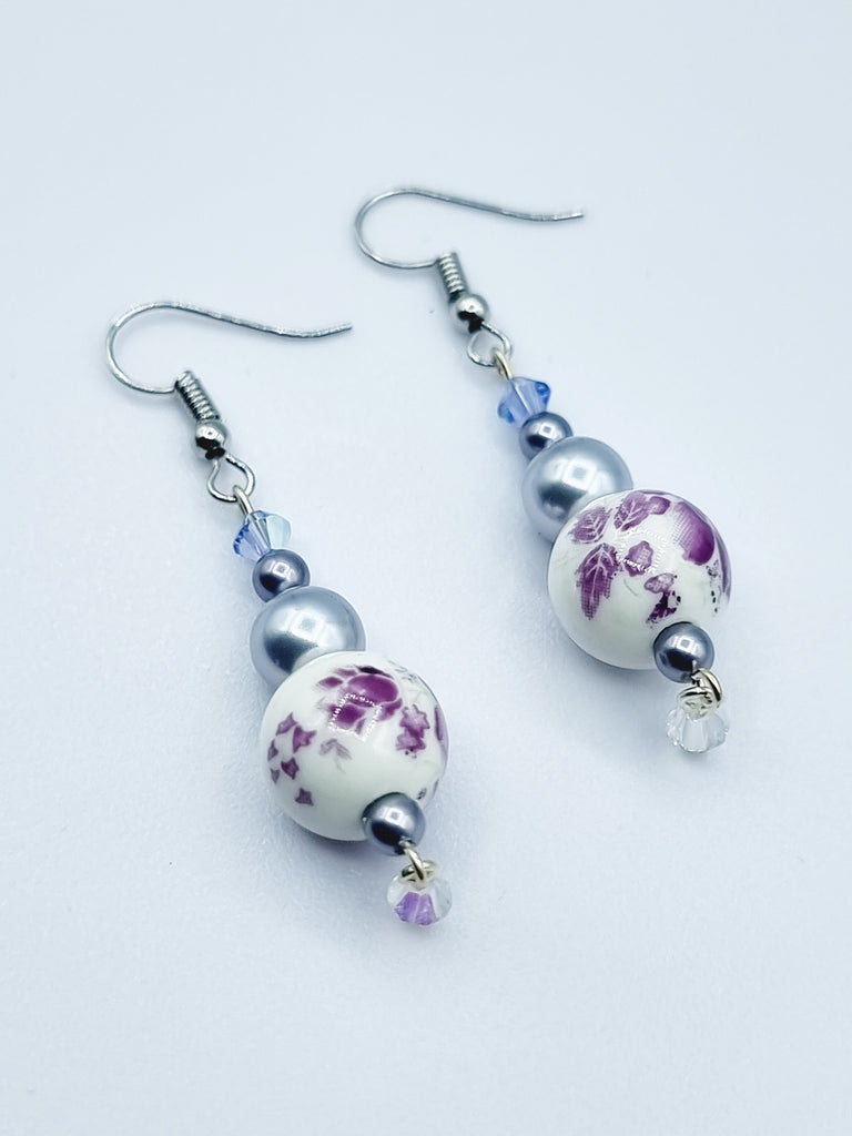 A pair of porcelain bead drop earrings, designed with Swarovski pearls and crystals in shades of purple.