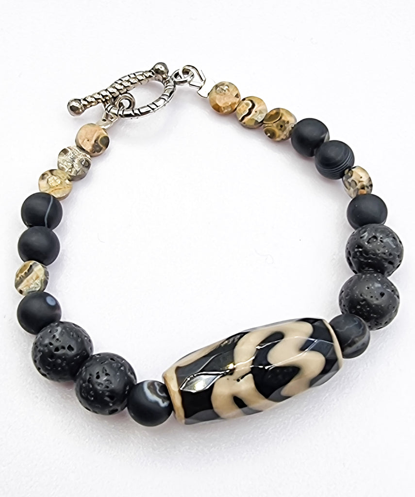 A stylish handmade unisex bracelet designed with a gorgeous Dzi Agate accent and combined with hues of black and brown in natural Lava Rock, Banded Onyx and Leopard Skin Jasper gemstones. An intricate and charming design, that makes a captivatingly unique statement piece. 