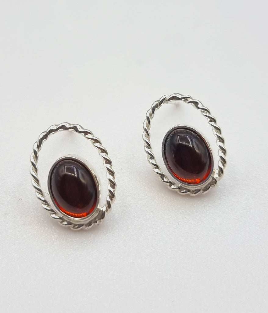 A floating style natural Baltic Amber stud earrings, delicately encased in a hollow twisted sterling silver bezel, in a tone of cherry red. Embrace sophistication and nature's beauty in this unique accessory, perfect for any occasion.  Origin of Amber: Poland