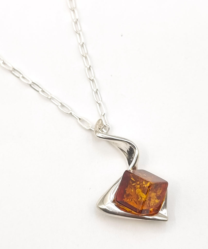 A unique cube shaped natural cognac Baltic Amber pendant set on an abstract swirl Sterling Silver ribbon. The origin of the Amber is Poland.