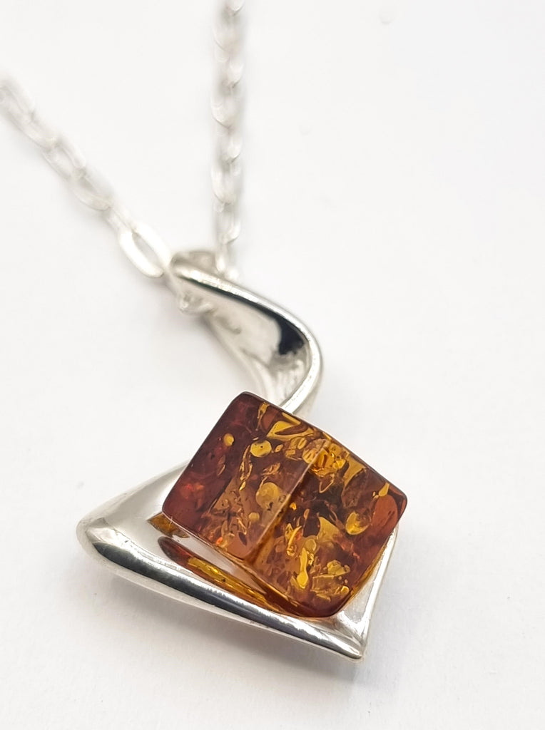 A unique cube shaped natural cognac Baltic Amber pendant set on an abstract swirl Sterling Silver ribbon. The origin of the Amber is Poland.